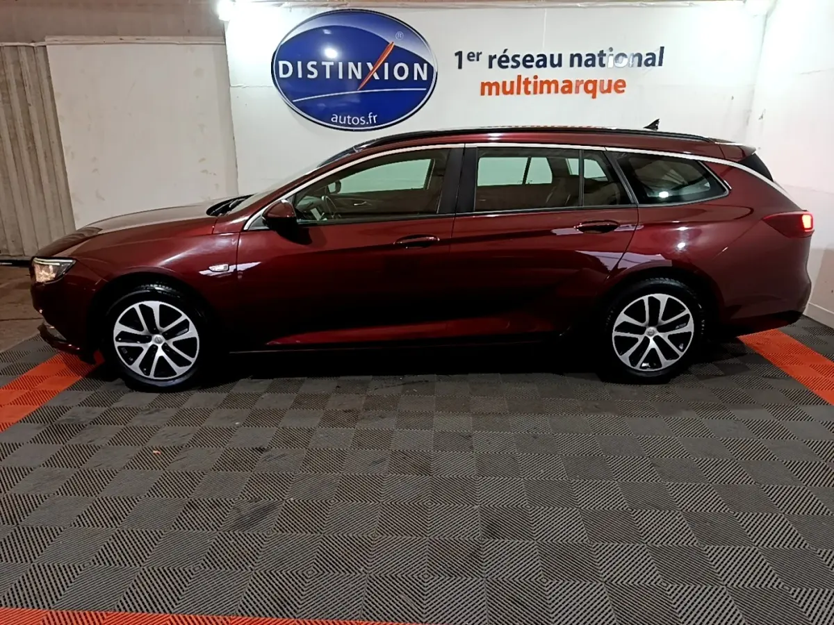 Opel Insignia break rouge vue de profil côté gauche, stationnée en intérieur sur sol damier.