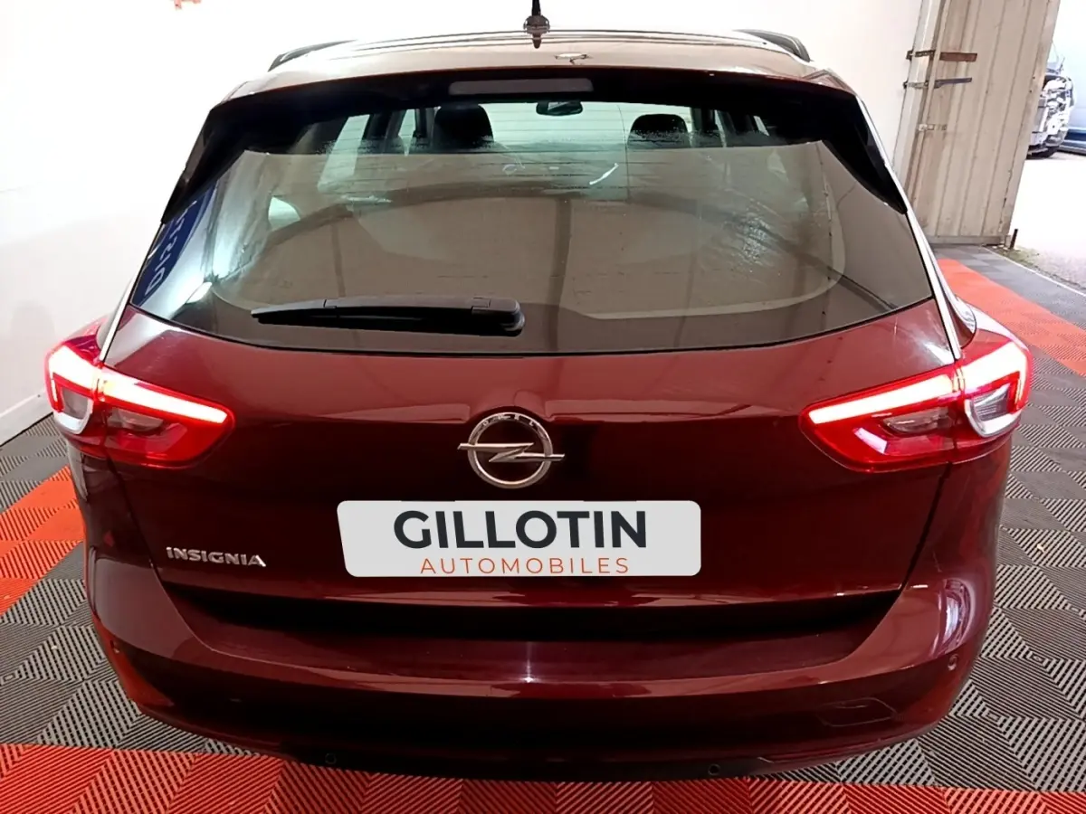 Vue arrière d'une Opel Insignia rouge avec feux allumés dans un garage au sol rouge et noir.