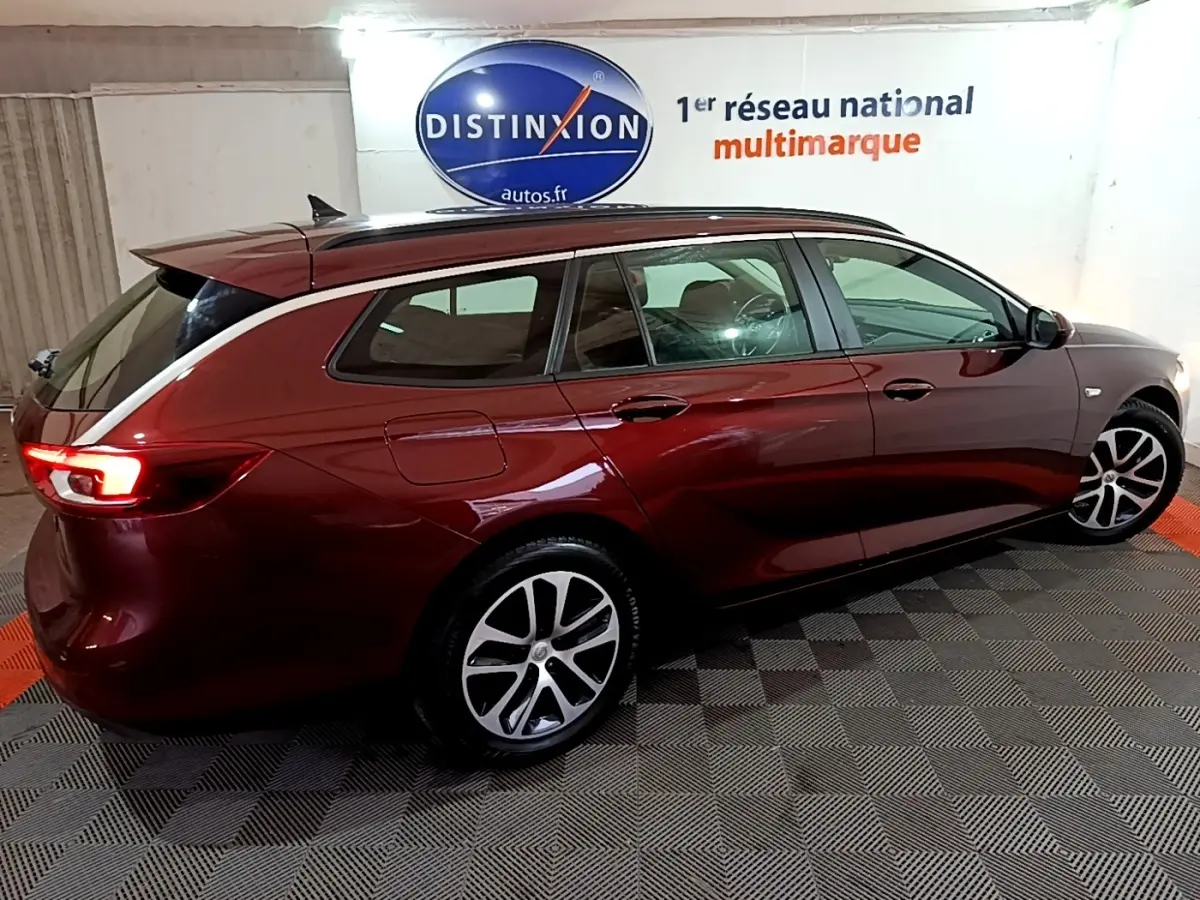 Opel Insignia rouge vue de profil côté droit, break avec jantes alliage et feux arrière allumés.