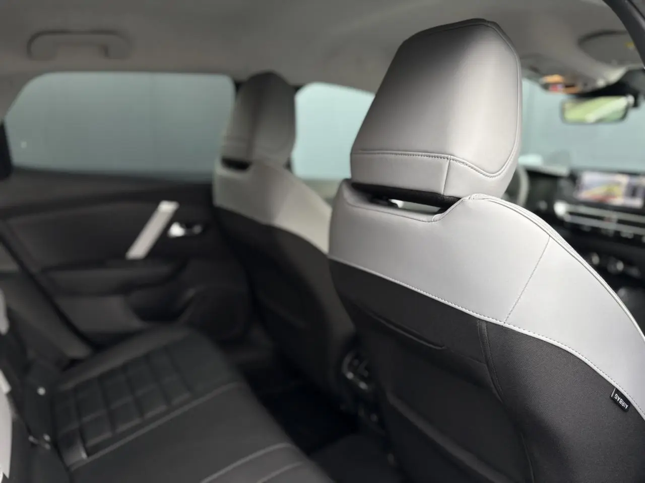 Vue intérieure arrière droite montrant les sièges bicolores gris clair et noir du Citroën C4 Hybrid 2025.