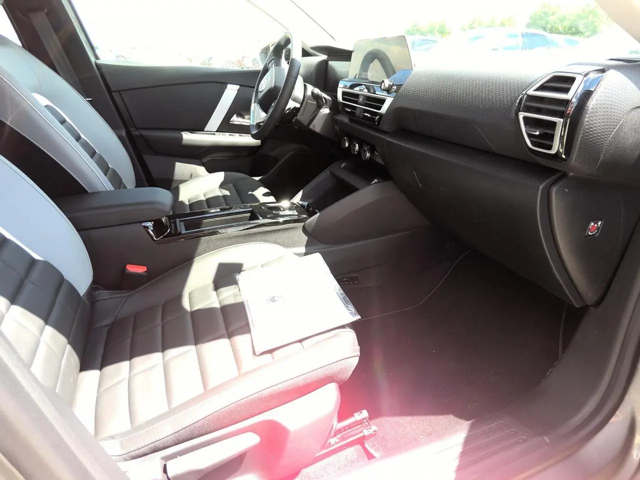 Vue intérieure côté passager avant de la Citroën C4 Hybrid 2025 avec sièges bi-ton gris et noir et tableau de bord moderne.