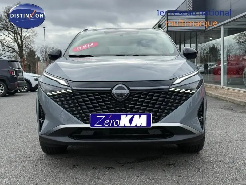 Vue frontale du Nissan Qashqai Hybrid e-POWER 2025 en gris Argile avec calandre noire et feux LED distinctifs allumés.
