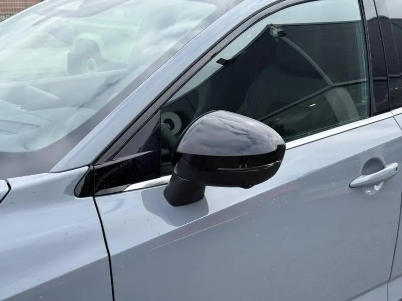 Gros plan sur le rétroviseur noir côté gauche du Nissan Qashqai Hybrid e-POWER 2025 en Gris Argile, avec porte et vitre visibles.