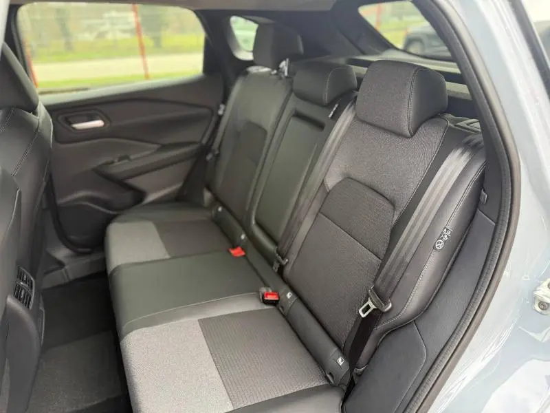 Vue intérieure arrière droite du Nissan Qashqai Hybrid e-POWER 2025, sièges tissu noir et gris, ceinture de sécurité visible.