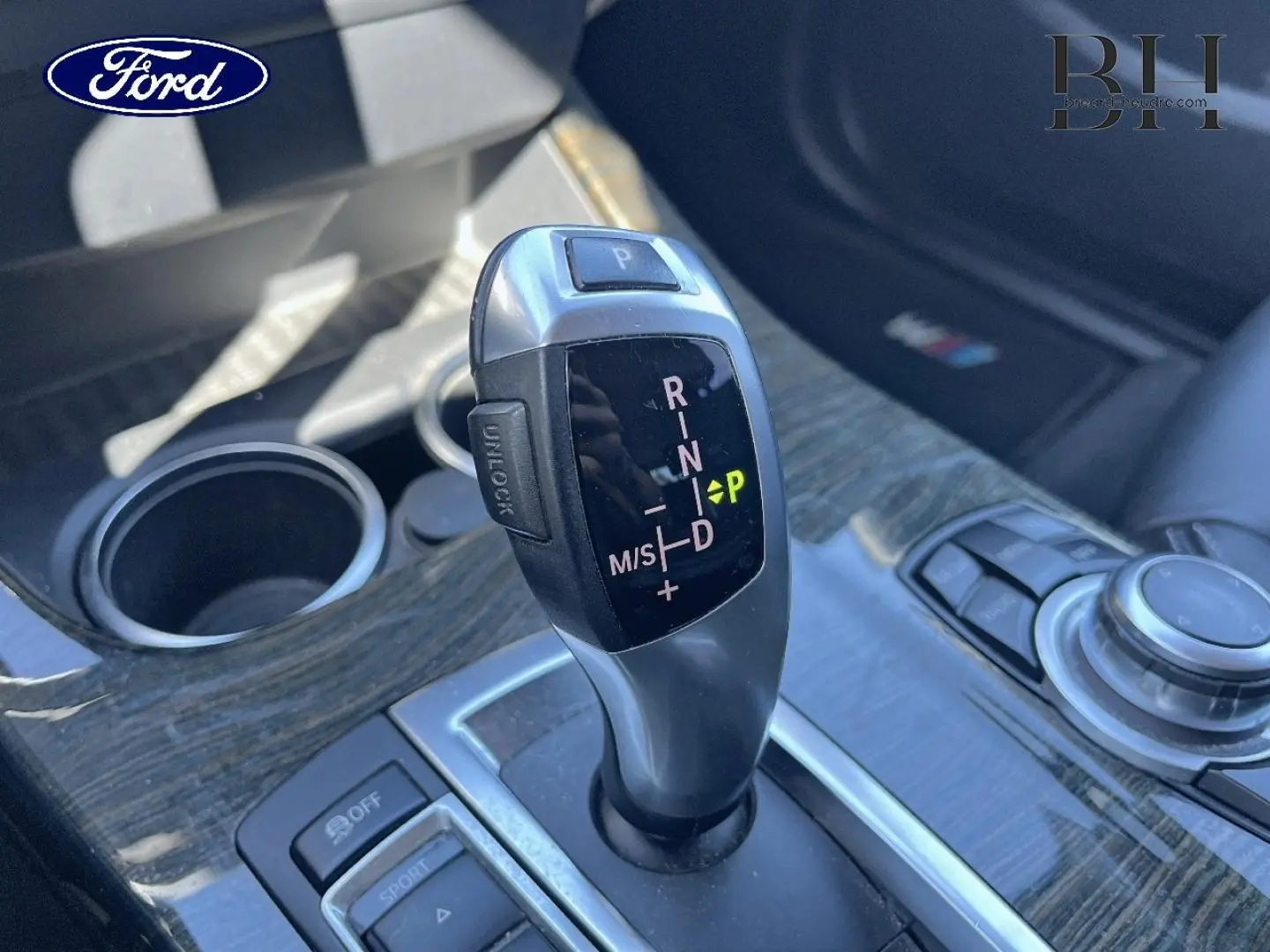Levier de vitesse automatique BMW xDrive20dA en gros plan sur console bois, avec commandes et porte-gobelets visibles.