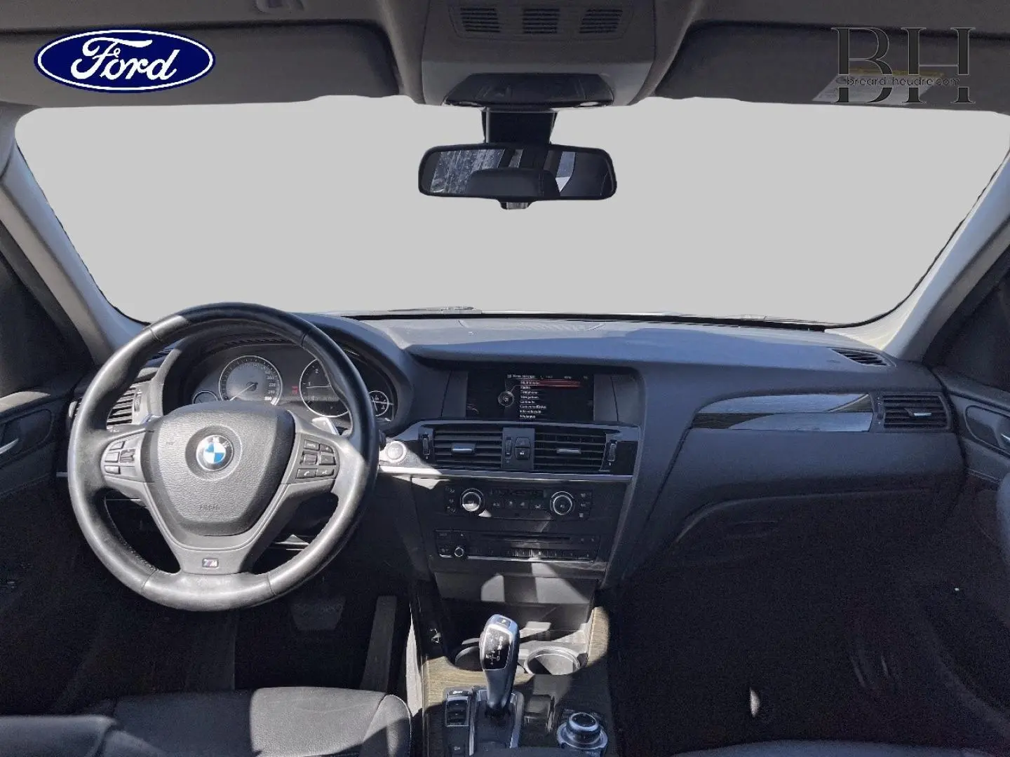 Intérieur BMW X3 2013 vu de face, tableau de bord noir avec volant cuir et levier de vitesse automatique.