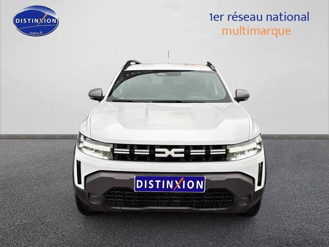 Vue avant du Dacia Duster blanc arctic avec calandre noire et phares LED allumés sur fond neutre.