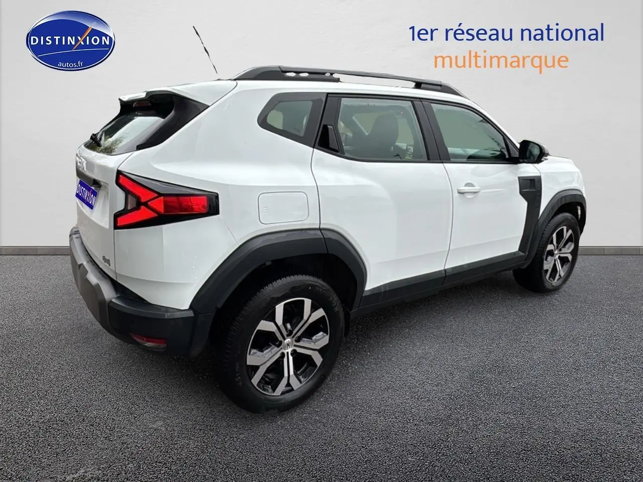 Vue 3/4 arrière droite d'un Dacia Duster blanc arctic avec barres de toit et jantes alu visibles.