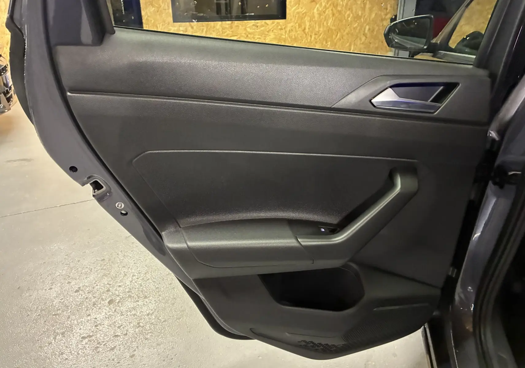 Porte arrière droite ouverte d'une Volkswagen Polo gris 2025, intérieur noir avec poignée et commande de vitre visible.