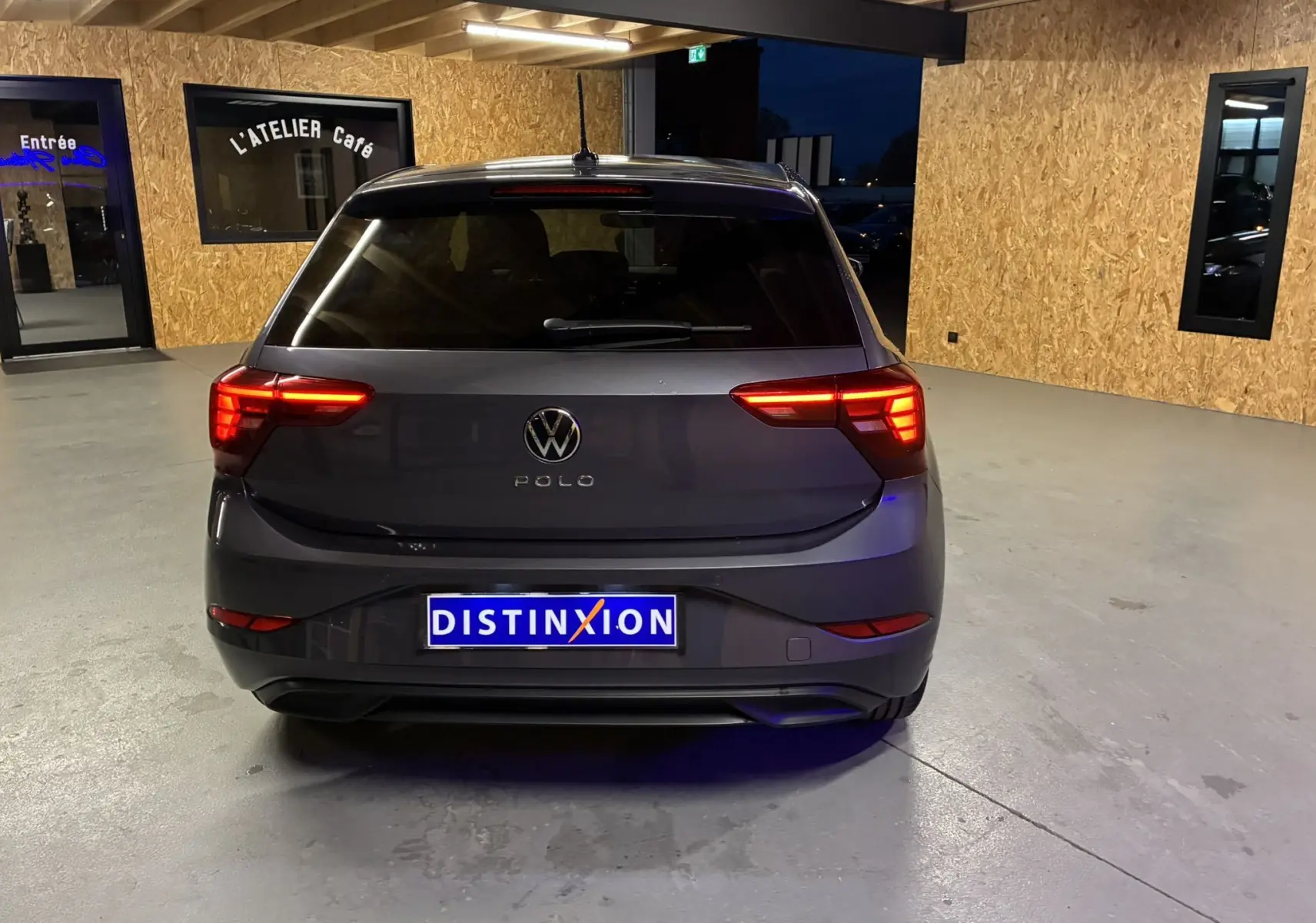 Vue arrière d'une Volkswagen Polo gris foncé 2025 avec feux allumés dans un garage éclairé.