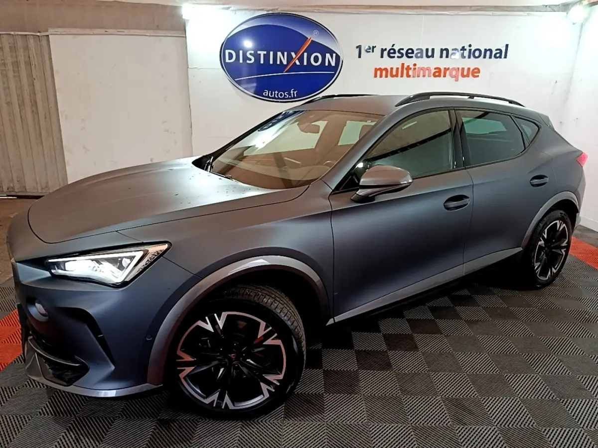 CUPRA Formentor gris foncé en 3/4 avant droit, avec jantes noires et phares LED allumés en intérieur showroom.