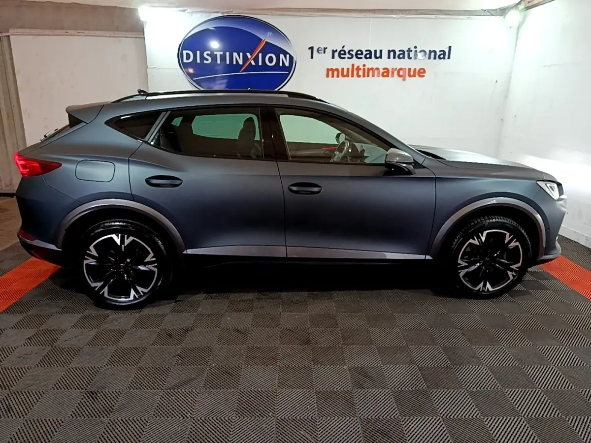 Vue de profil côté gauche d’un CUPRA Formentor gris foncé 2024 avec jantes noires et toit ouvrant en intérieur showroom.