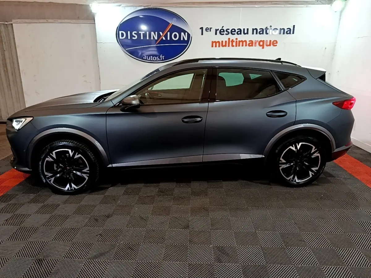 Vue de profil côté gauche d’un CUPRA Formentor gris foncé 2024 avec jantes noires à motifs blancs dans un showroom.