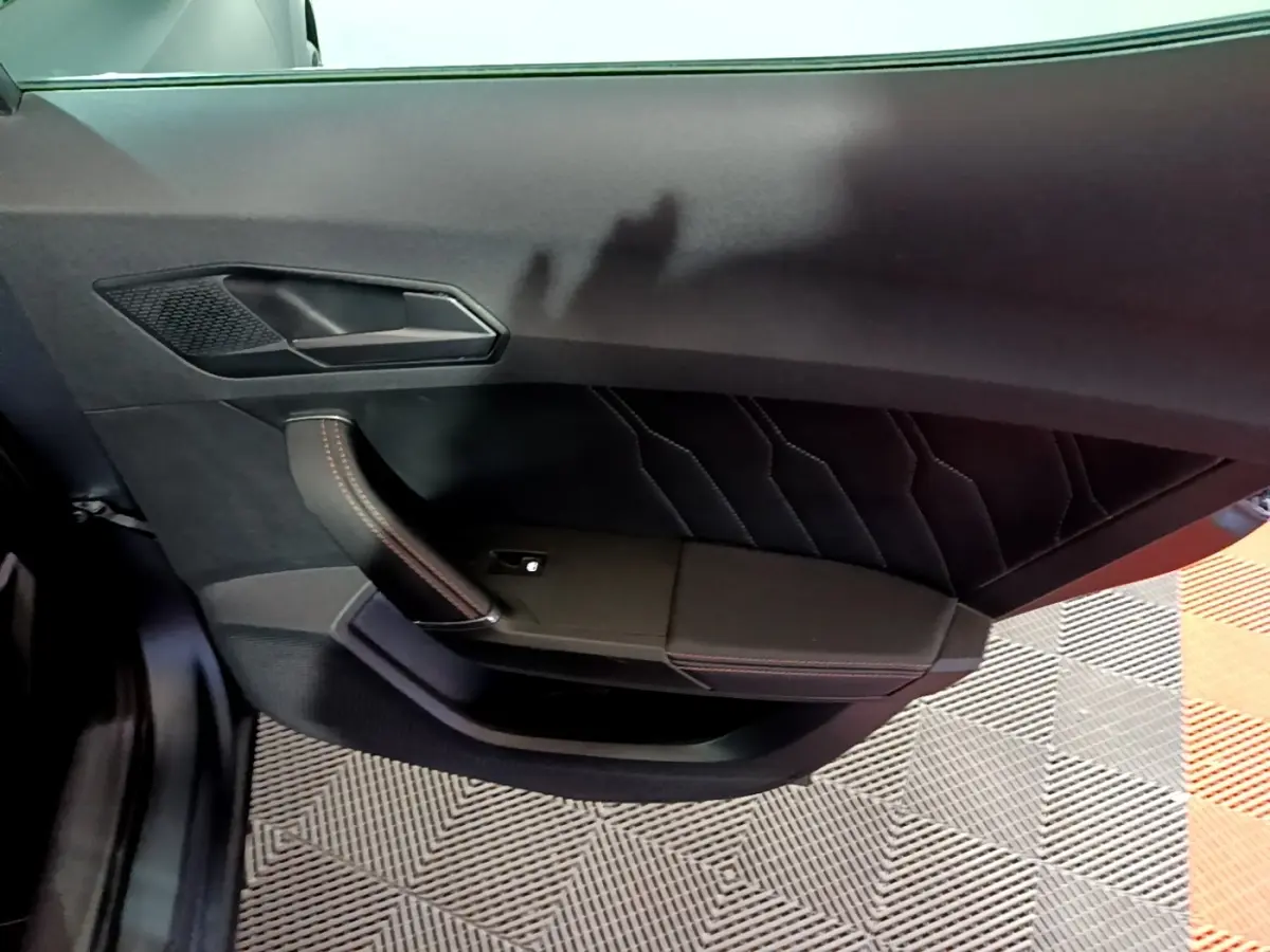 Vue intérieure de la porte avant gauche de la CUPRA Formentor gris foncé, avec surpiqûres rouges et poignée design.