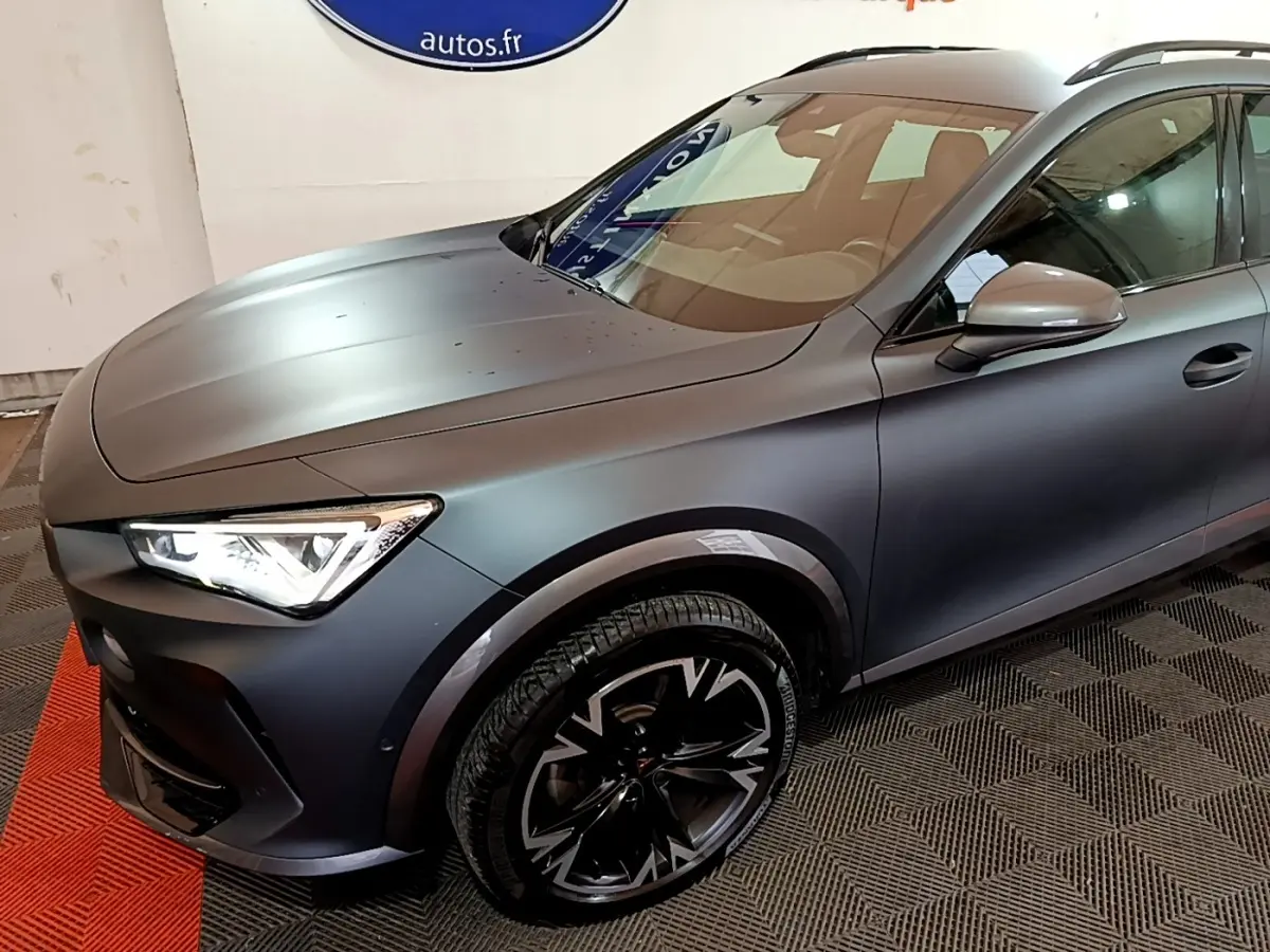 Vue 3/4 avant droit d'une CUPRA Formentor gris foncé avec jantes noires à motifs argentés et phares allumés.