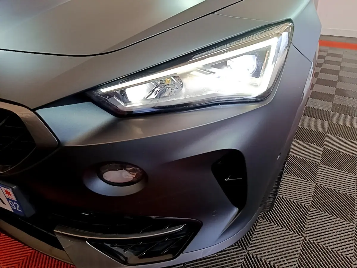 Gros plan sur l'avant droit d'une CUPRA Formentor gris foncé, mettant en valeur le phare LED allumé et la calandre sportive.