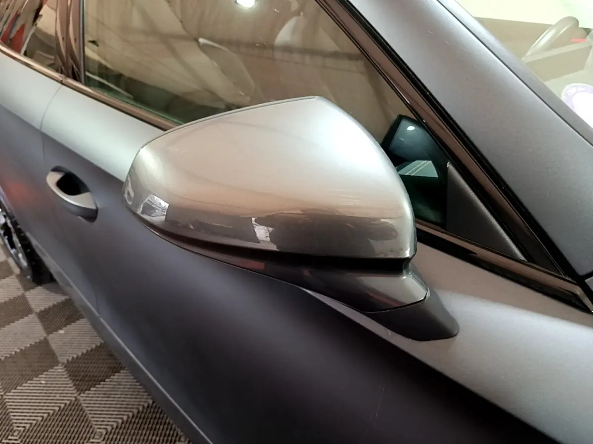 Gros plan sur le rétroviseur côté gauche d’un CUPRA Formentor gris foncé avec porte et vitre partiellement visibles.