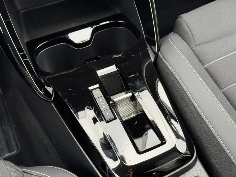 Gros plan sur la console centrale noire brillante de la Citroën C3 électrique 2025 avec levier de vitesses automatique et accoudoir tissu gris.