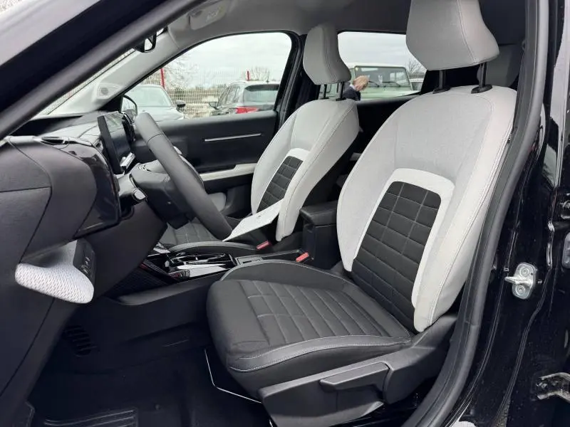 Vue intérieure côté gauche de la Citroën C3 électrique 2025 avec sièges bicolores gris clair et noir, volant et tableau de bord visibles.