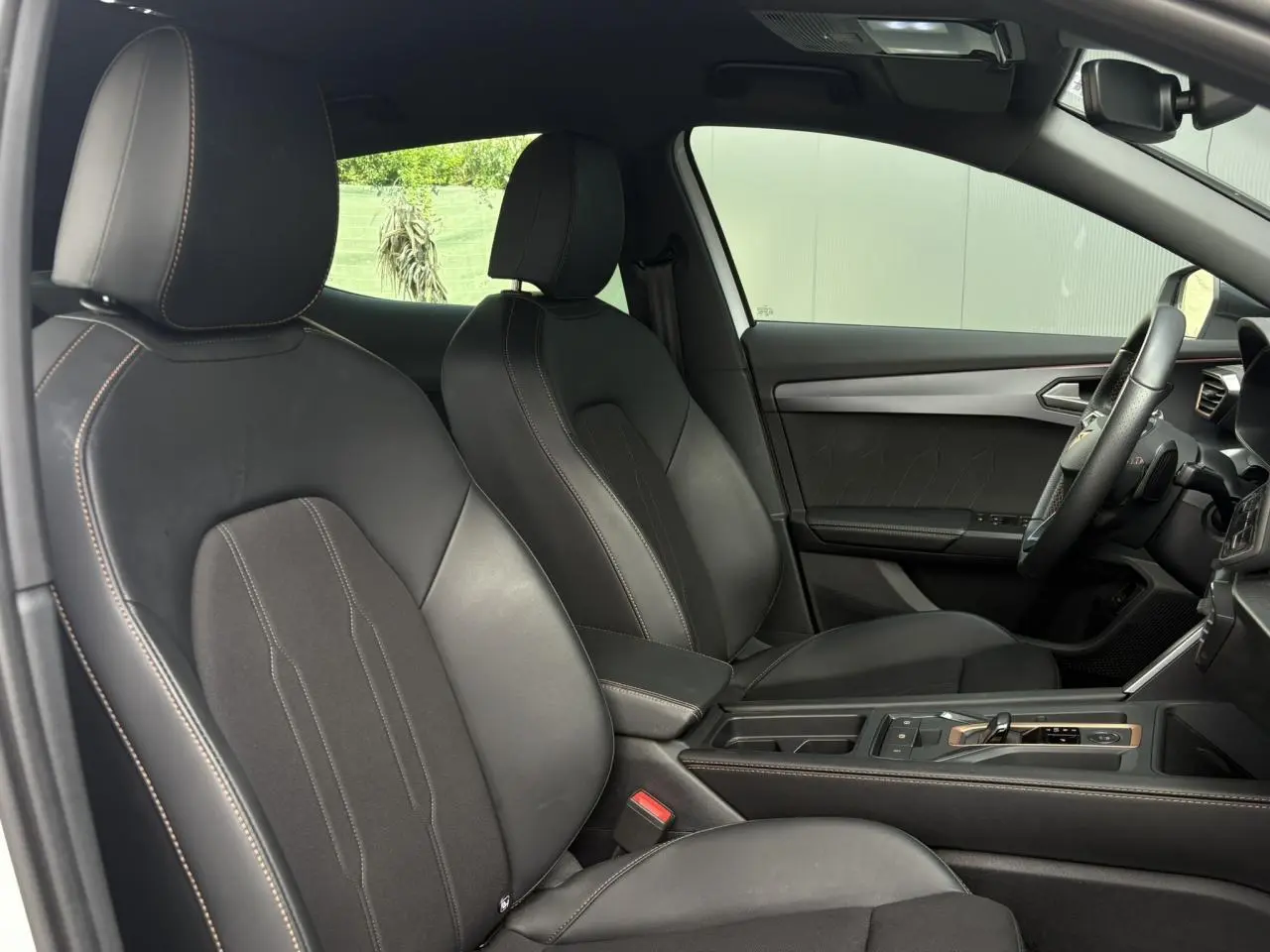 Vue intérieure côté conducteur du CUPRA Formentor 2025, sièges sports noirs avec surpiqûres et accoudoir central réglable.