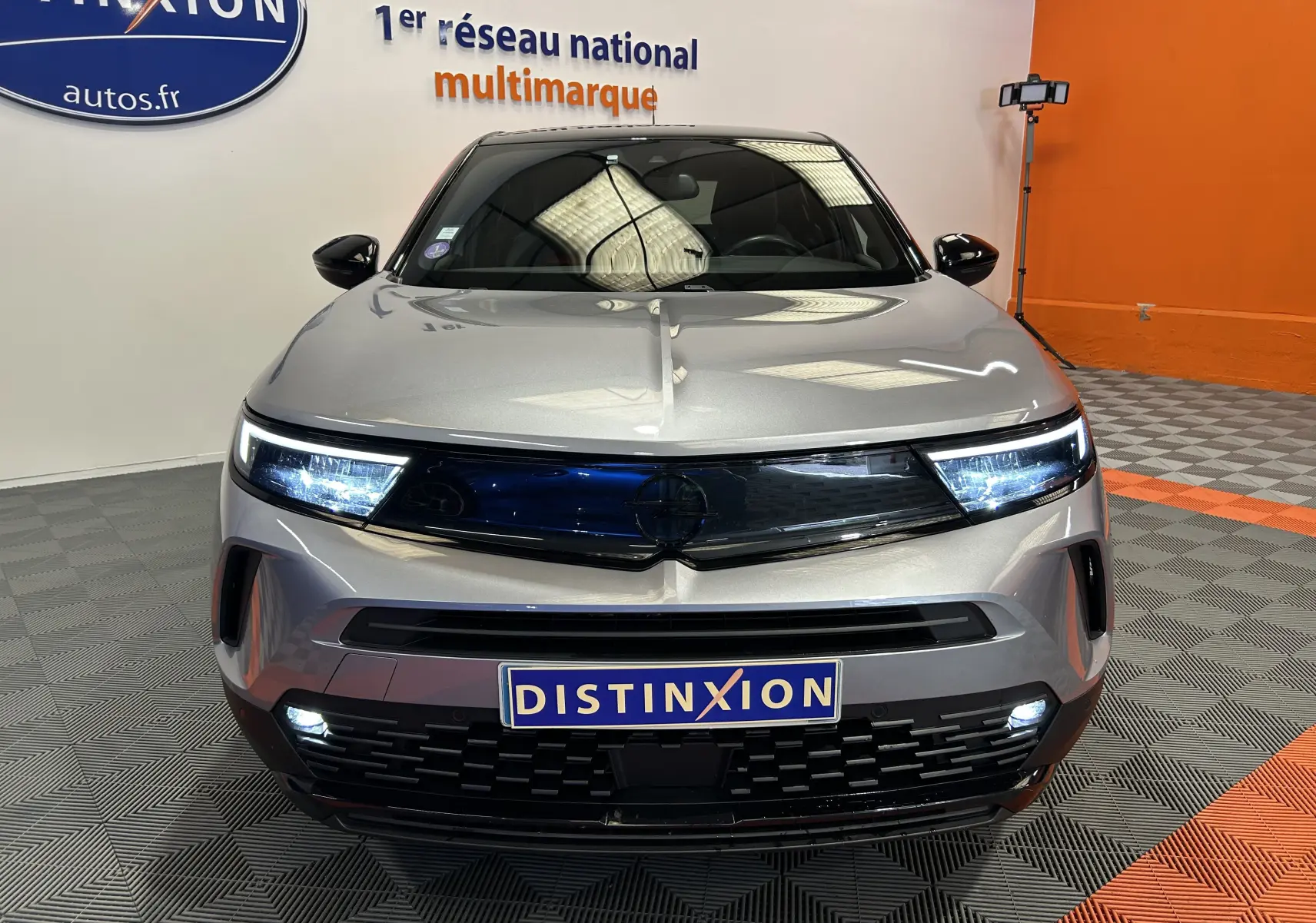 Vue avant d'un Opel Mokka GS Line gris avec phares LED allumés et plaque Distinxion dans un showroom.