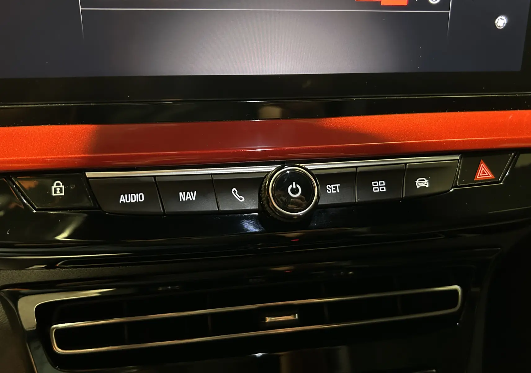 Gros plan sur la console centrale de l’Opel Mokka gris, avec boutons audio, navigation et alerte conducteur, finition rouge métallique.
