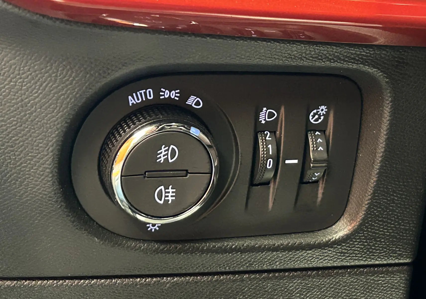 Gros plan sur les commandes d’éclairage et réglages de phares du tableau de bord noir d’un Opel Mokka gris.