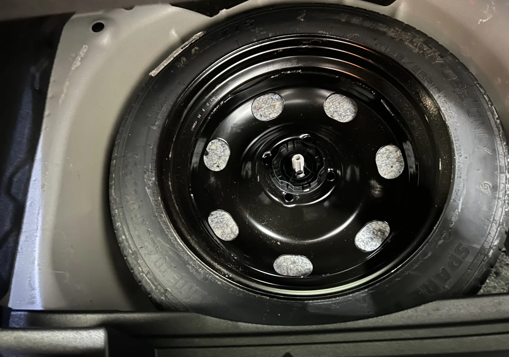 Gros plan sur la roue de secours noire dans le coffre d’un Opel Mokka gris, vue plongeante depuis l’arrière.