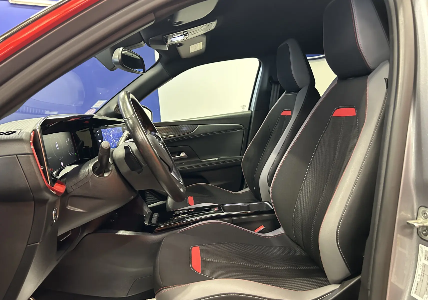 Vue intérieure côté gauche de l’Opel Mokka gris, mettant en valeur les sièges noirs avec surpiqûres rouges et le tableau de bord moderne.