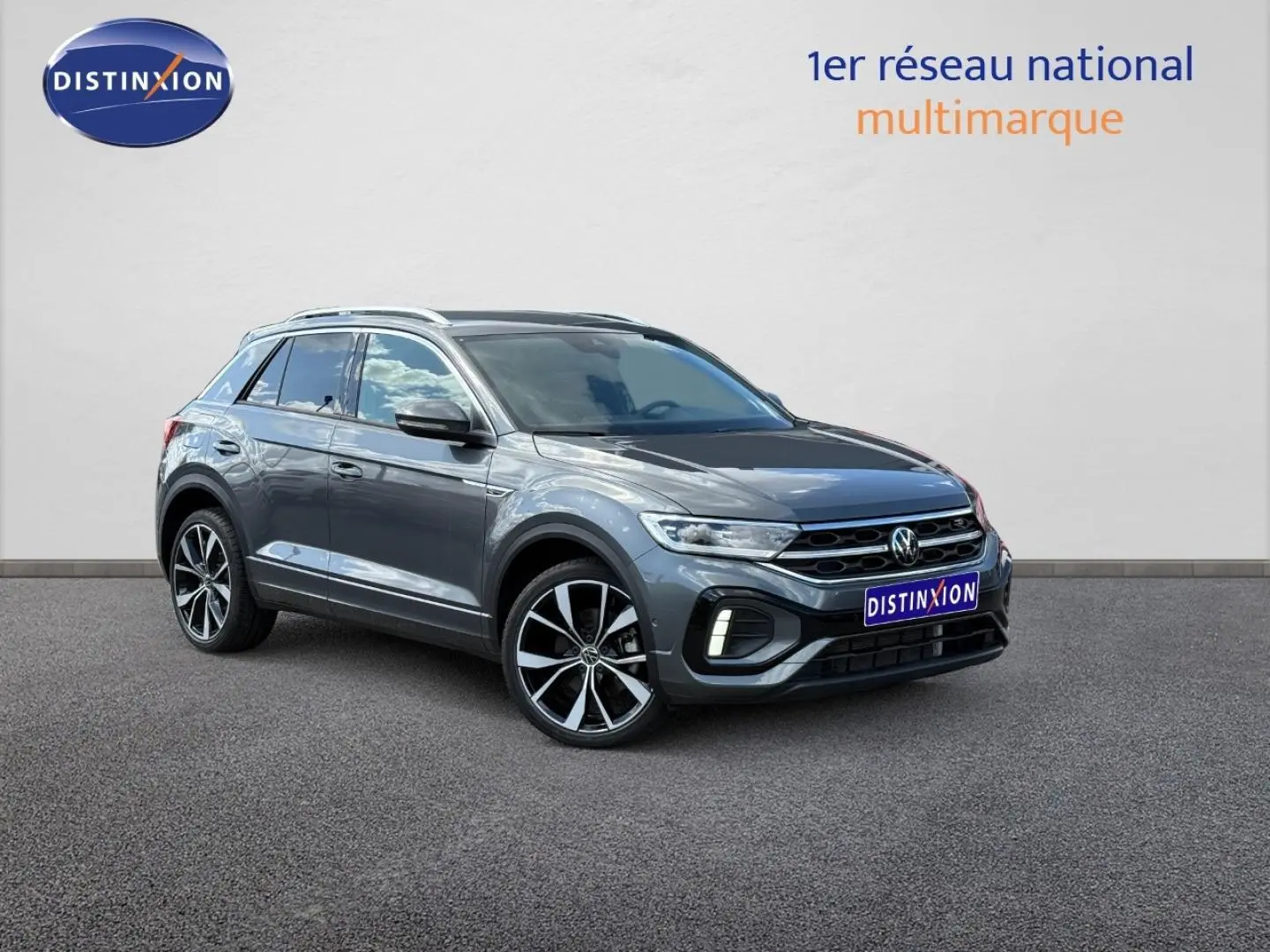 Volkswagen T-Roc gris Indium métallisé en 3/4 avant droit, avec jantes alliage et barres de toit visibles.