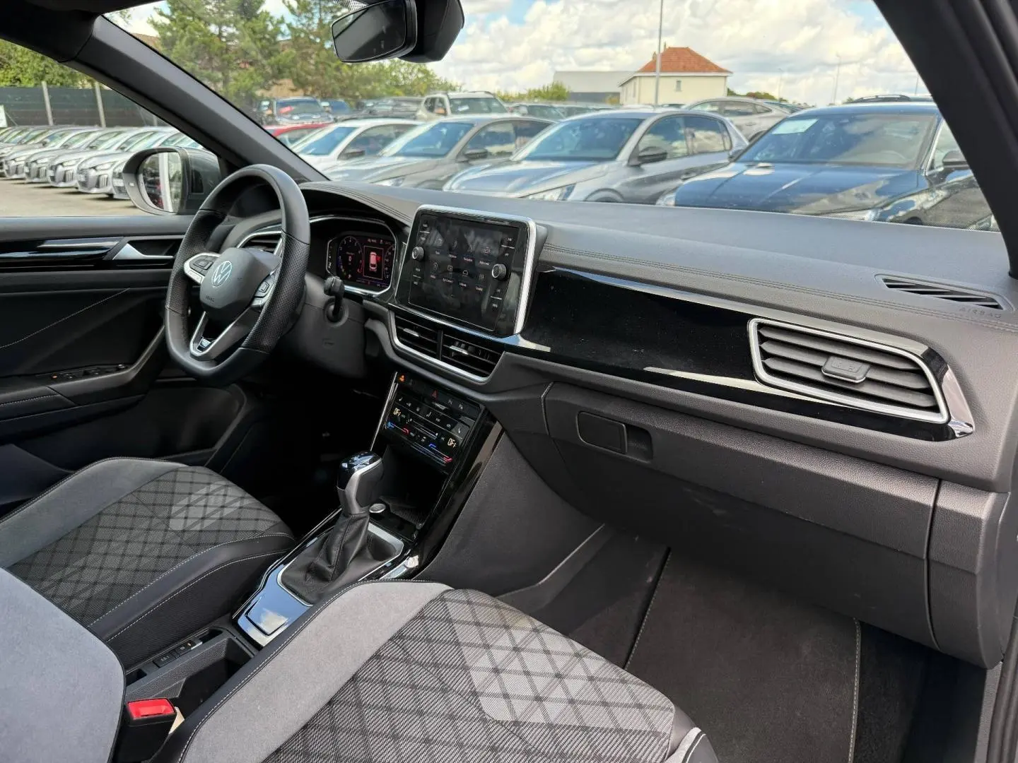 Vue intérieure avant droite du Volkswagen T-Roc 2025 avec sellerie gris artvelours et tableau de bord noir brillant.