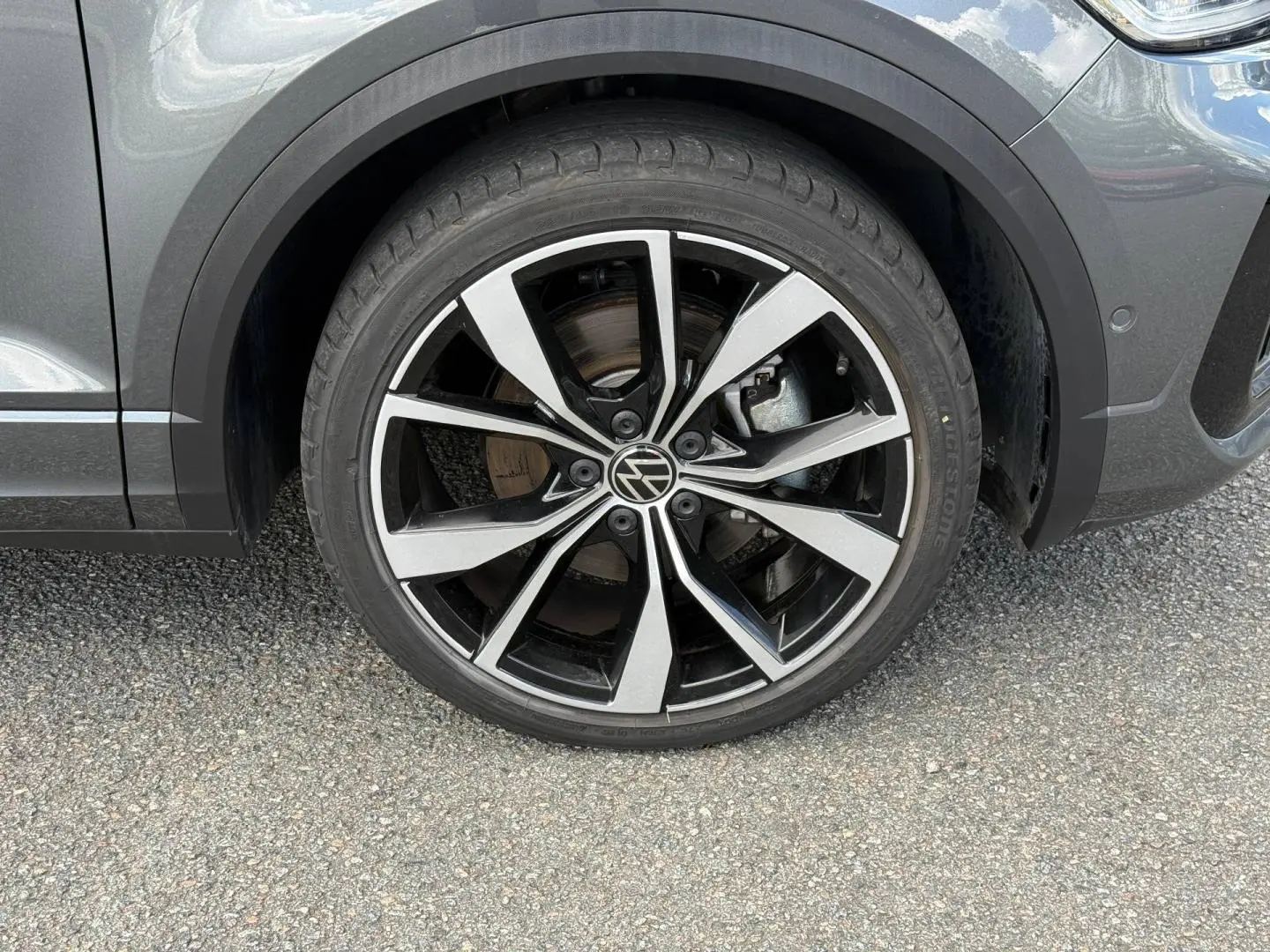 Gros plan sur la roue avant droite du Volkswagen T-Roc gris Indium métallisé avec jante alliage noire et argentée.