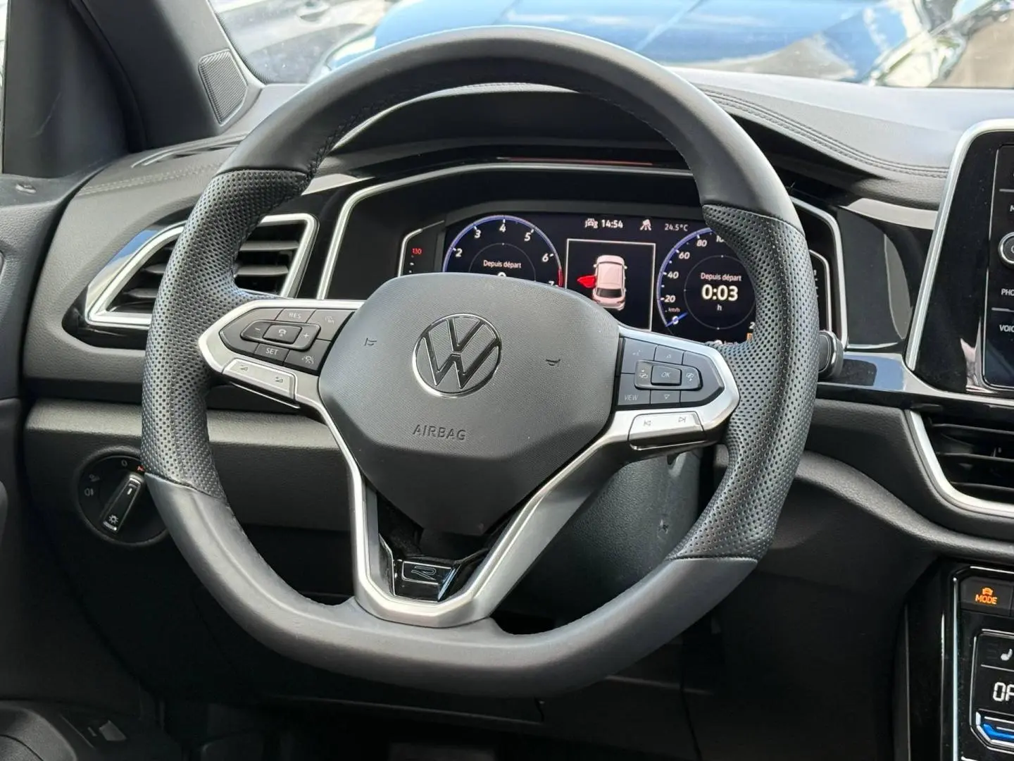 Vue rapprochée du volant multifonction noir et gris du Volkswagen T-Roc 2025 avec tableau de bord numérique en arrière-plan.