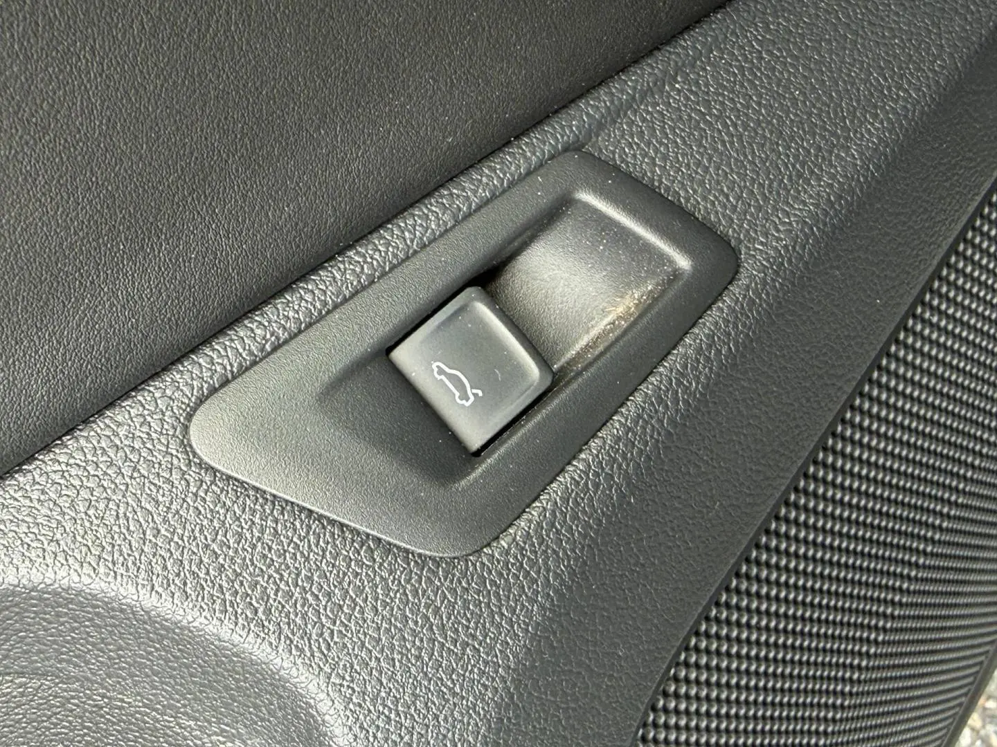 Bouton d'ouverture du coffre en plastique noir sur panneau intérieur texturé d'un Volkswagen T-Roc gris Indium.