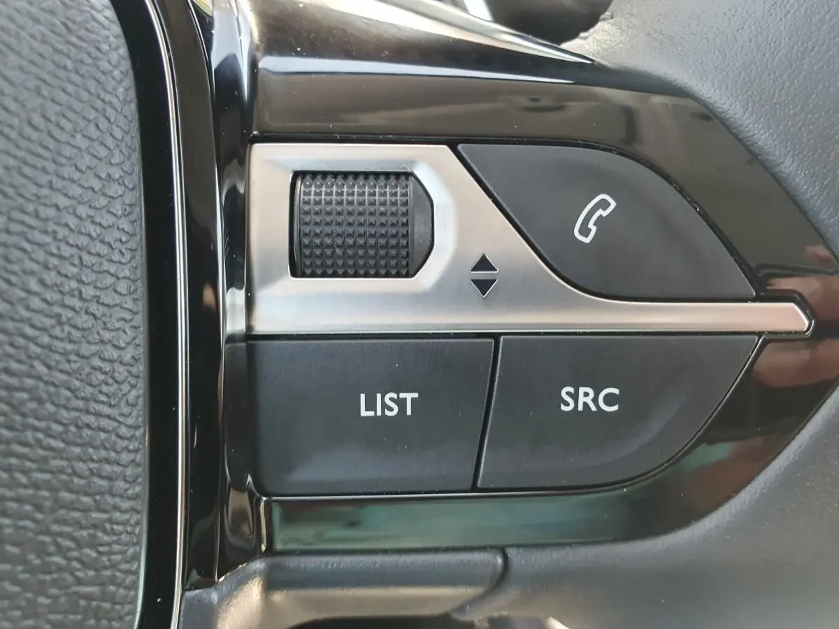Gros plan sur les commandes multimédia au volant côté gauche du Peugeot 208 gris Sellenium 2025.