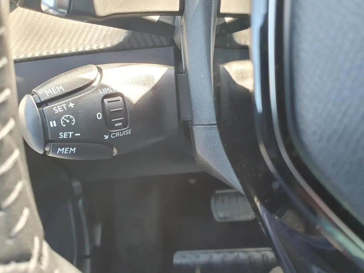 Gros plan sur la commande de régulateur de vitesse à gauche du volant dans l’habitacle d’une Peugeot 208 gris Sellenium.