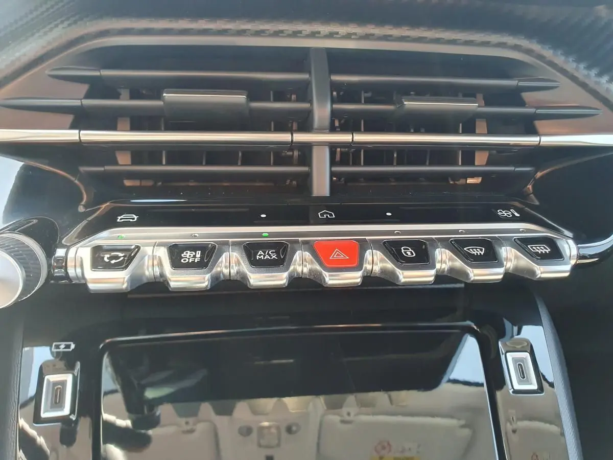 Vue rapprochée de la console centrale noire brillante avec boutons argentés et rouge dans une Peugeot 208 gris Sellenium.