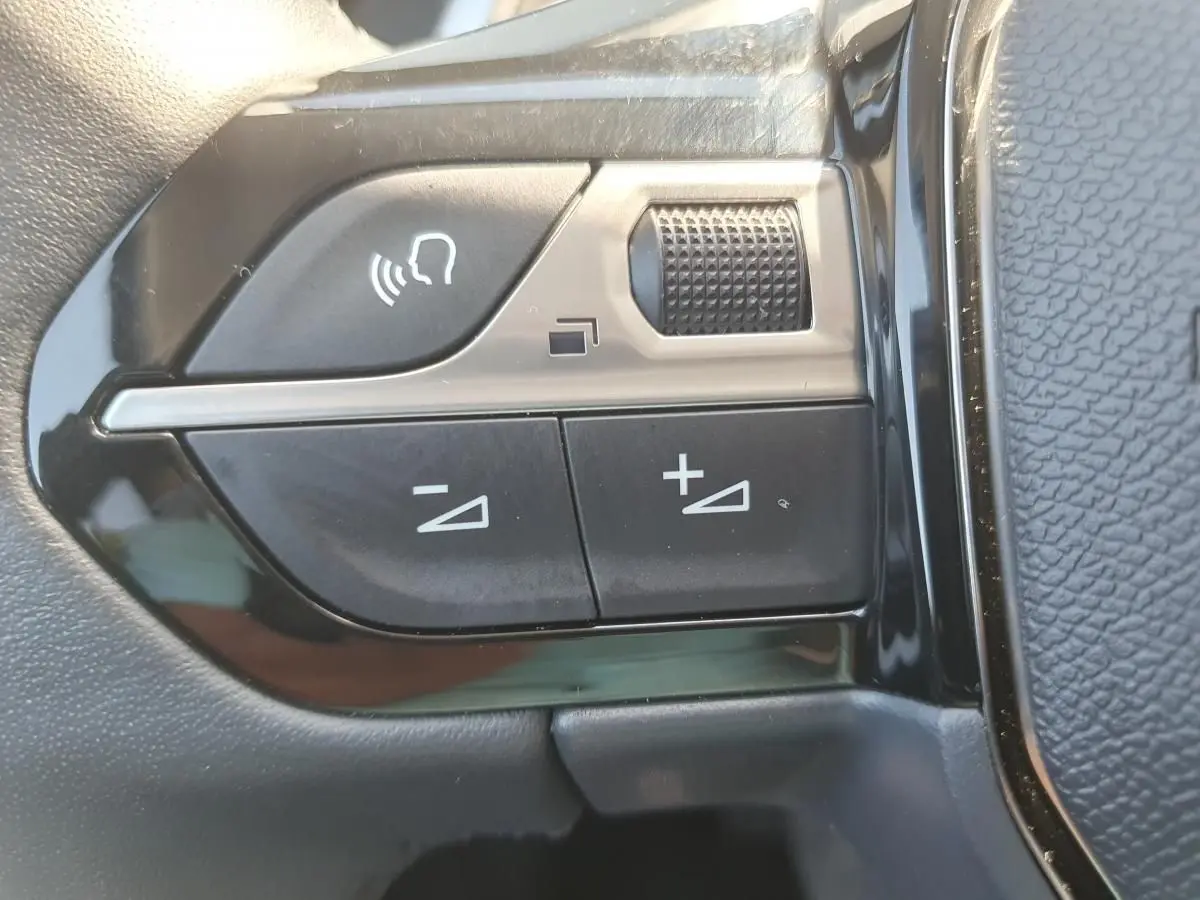 Gros plan sur les commandes de volume et de reconnaissance vocale sur le volant noir du Peugeot 208 gris Sellenium 2025.