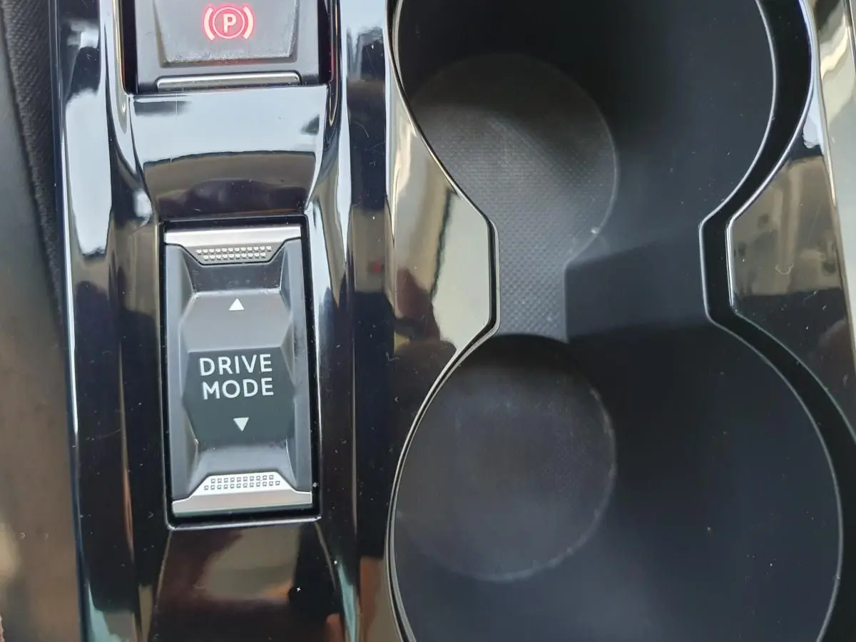 Gros plan sur la console centrale noire brillante de la Peugeot 208 1.2 Hybrid avec bouton Drive Mode et porte-gobelets.