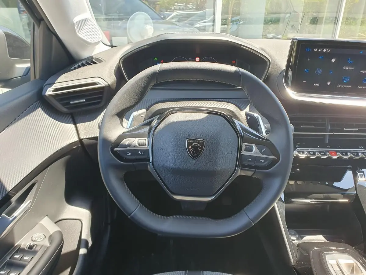Vue intérieure centrée sur le volant cuir noir et le tableau de bord moderne de la Peugeot 208 1.2 Hybrid 110 Allure.
