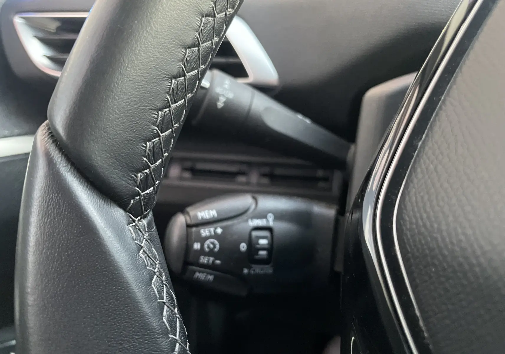 Gros plan sur la commande de régulateur de vitesse derrière le volant noir du Peugeot 3008 blanc nacré, version 2019.