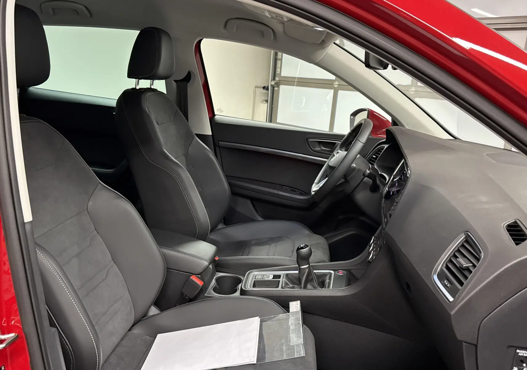 Vue intérieure côté conducteur du SEAT Ateca rouge velvet 2024, montrant sièges noirs et console centrale avec boîte manuelle.