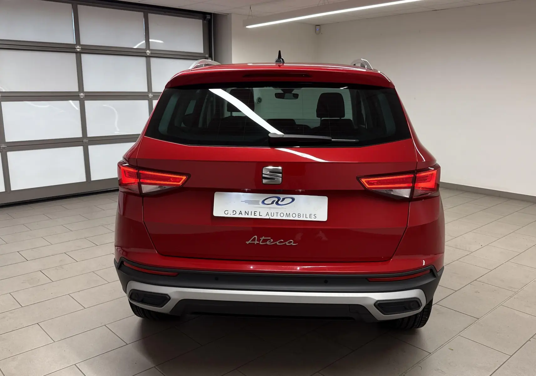 Vue arrière d'un SEAT Ateca 2024 rouge velvet, avec feux allumés et logo distinctif sur hayon.