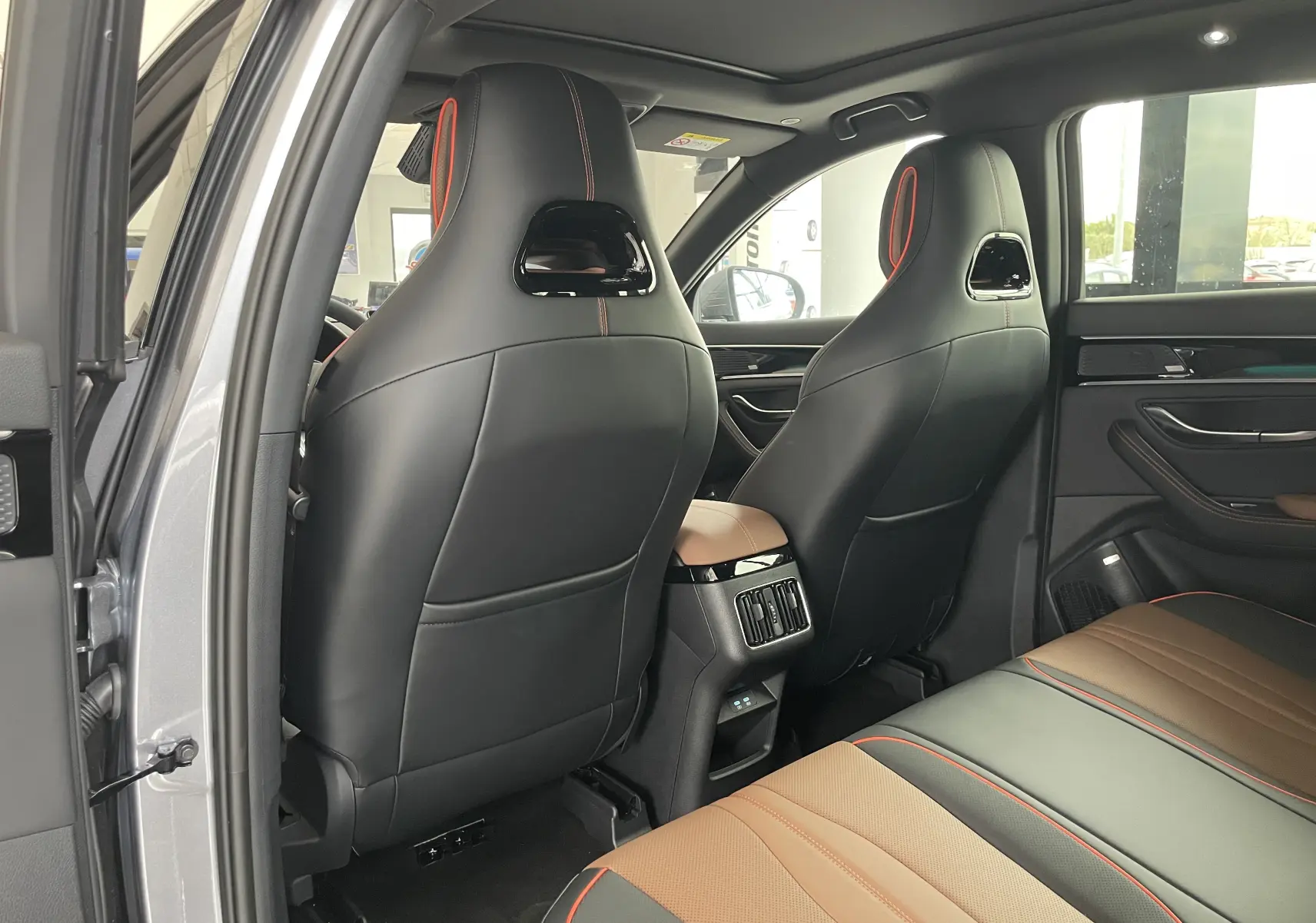 Vue intérieure arrière du BYD SEAL U 2026 en TIME GREY, sièges cuir noir et marron avec surpiqûres rouges et toit ouvrant panoramique.