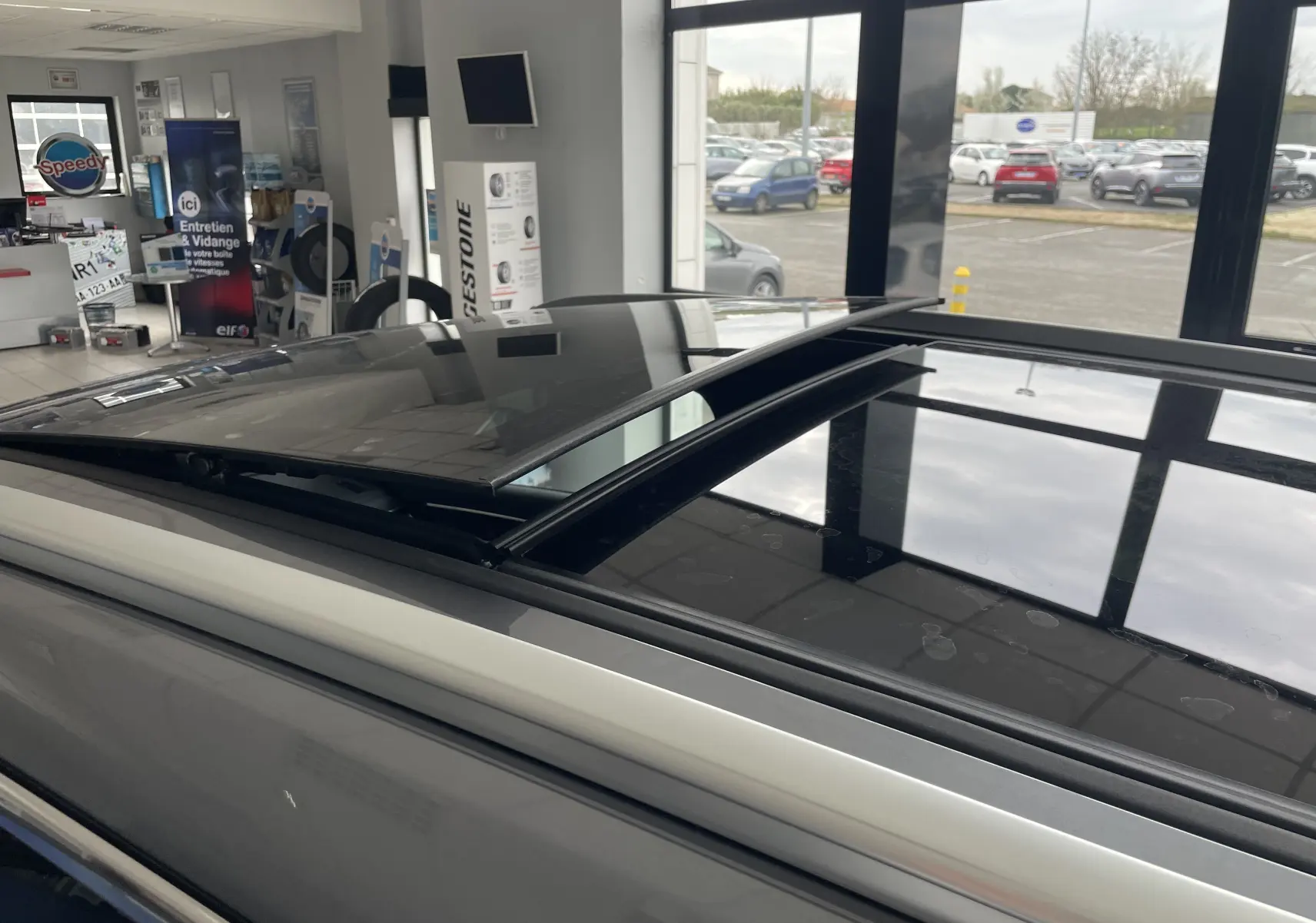 Vue rapprochée du toit ouvrant panoramique ouvert sur le côté gauche d’un BYD SEAL U gris TIME GREY en showroom.