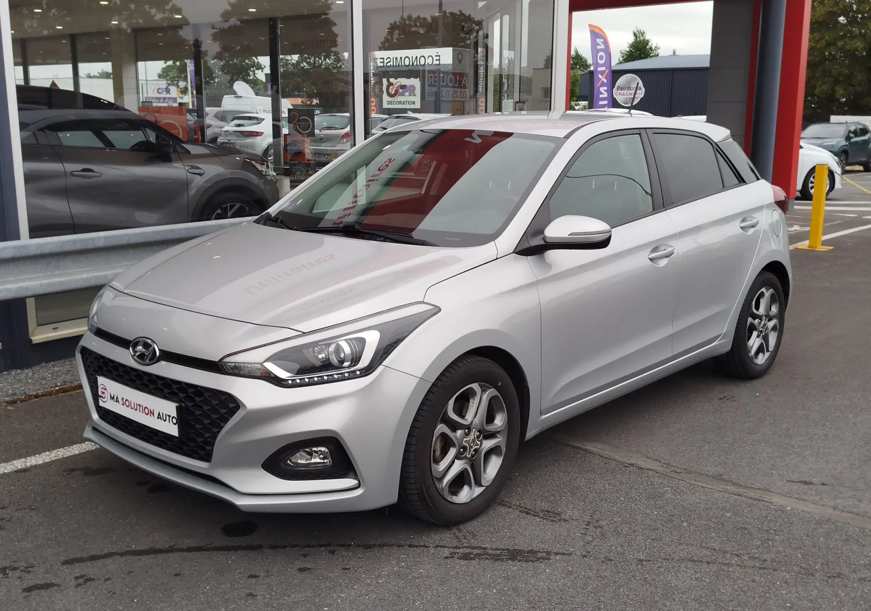 Vue 3/4 avant droite d'une Hyundai i20 2018 gris argent métallisé avec jantes alliage et calandre hexagonale noire.