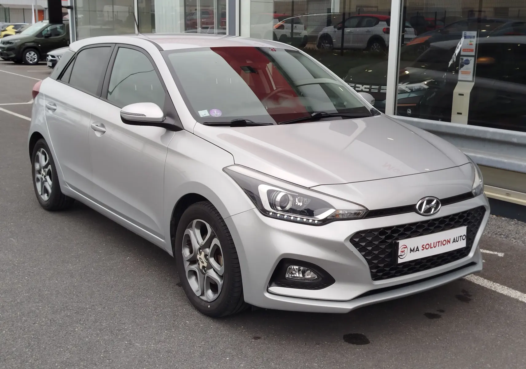 Vue 3/4 avant droite d'une Hyundai i20 2018 gris argenté avec calandre noire et phares LED distinctifs.