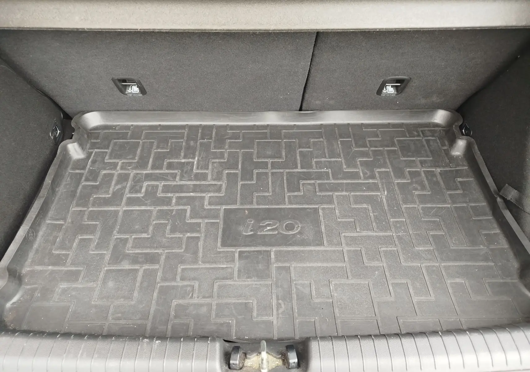 Vue intérieure du coffre d'une Hyundai i20 avec tapis de sol en caoutchouc noir marqué "i20" au centre.