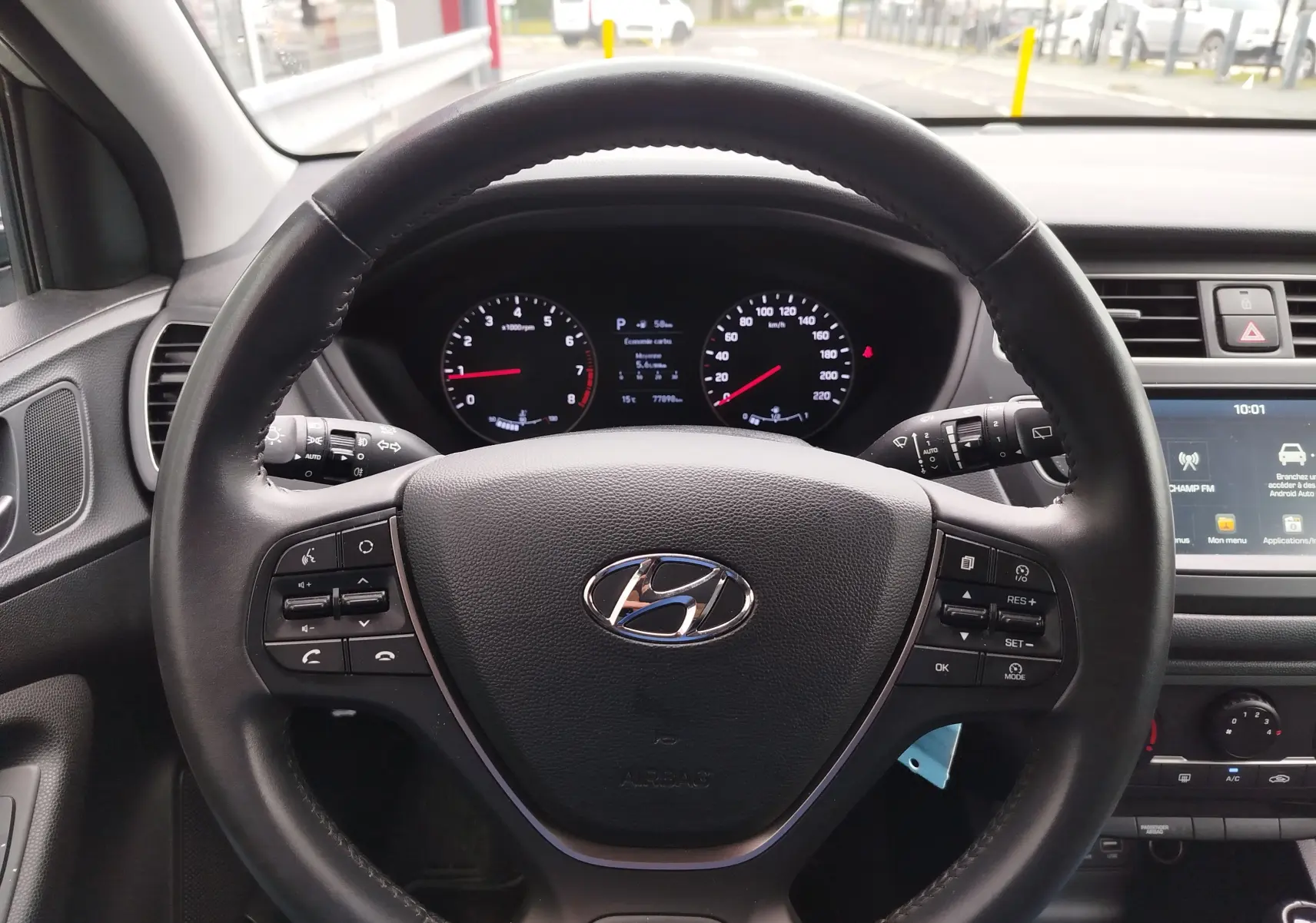 Vue intérieure centrée sur le volant noir de la Hyundai i20 2018, avec tableau de bord et écran tactile visibles.