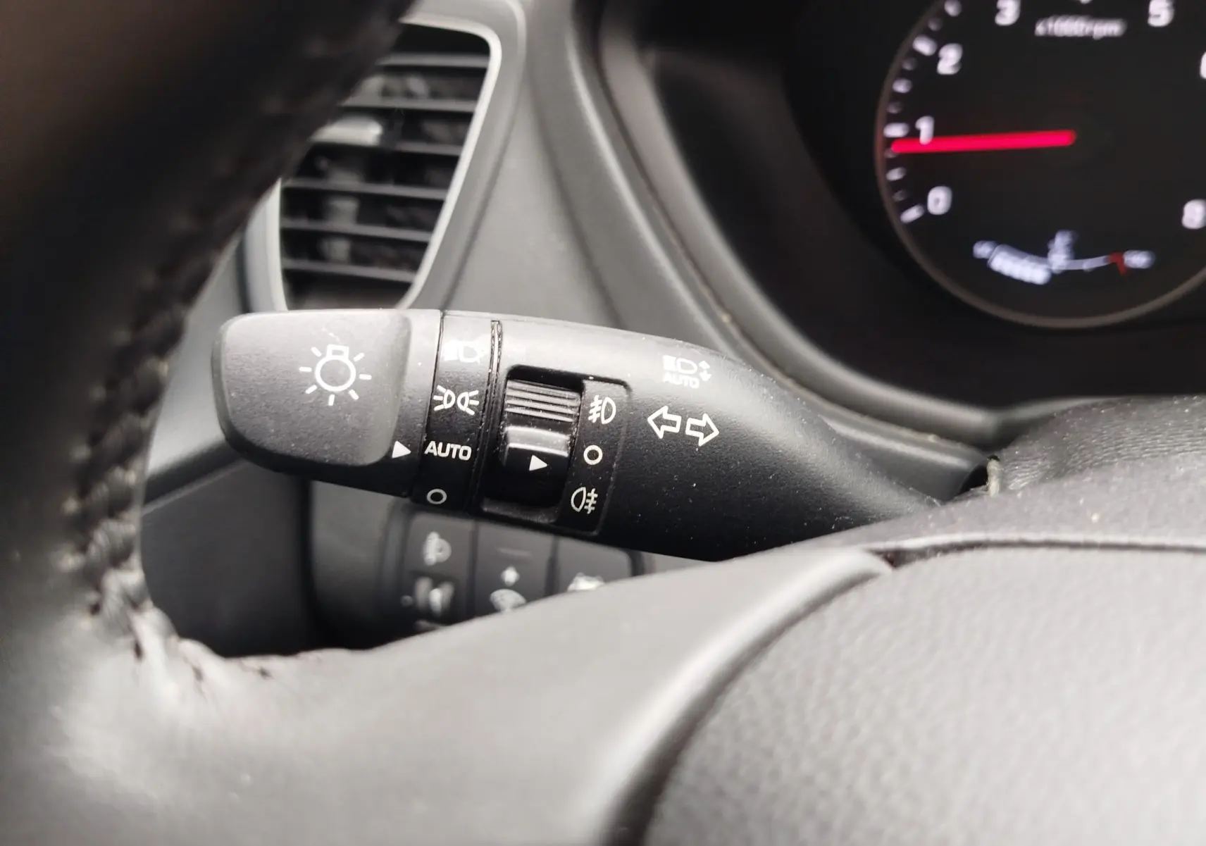 Gros plan sur la manette des feux et clignotants à gauche du volant d’une Hyundai i20 gris intérieur, avec tableau de bord partiellement visible.